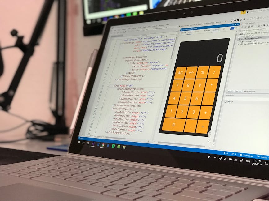 Close-up view of a silver laptop on a desk, displaying a code editor with lines of HTML and CSS on the left side and a bright orange calculator app with black and white symbols on the right side. The